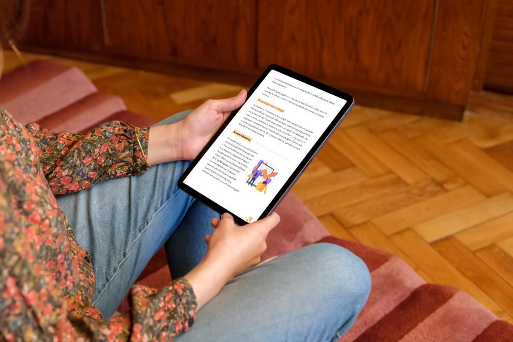 Donna seduta sul divano mentre legge una guida digitale al budgeting personale su tablet, con contenuti su strumenti per gestire le finanze in modo intuitivo.