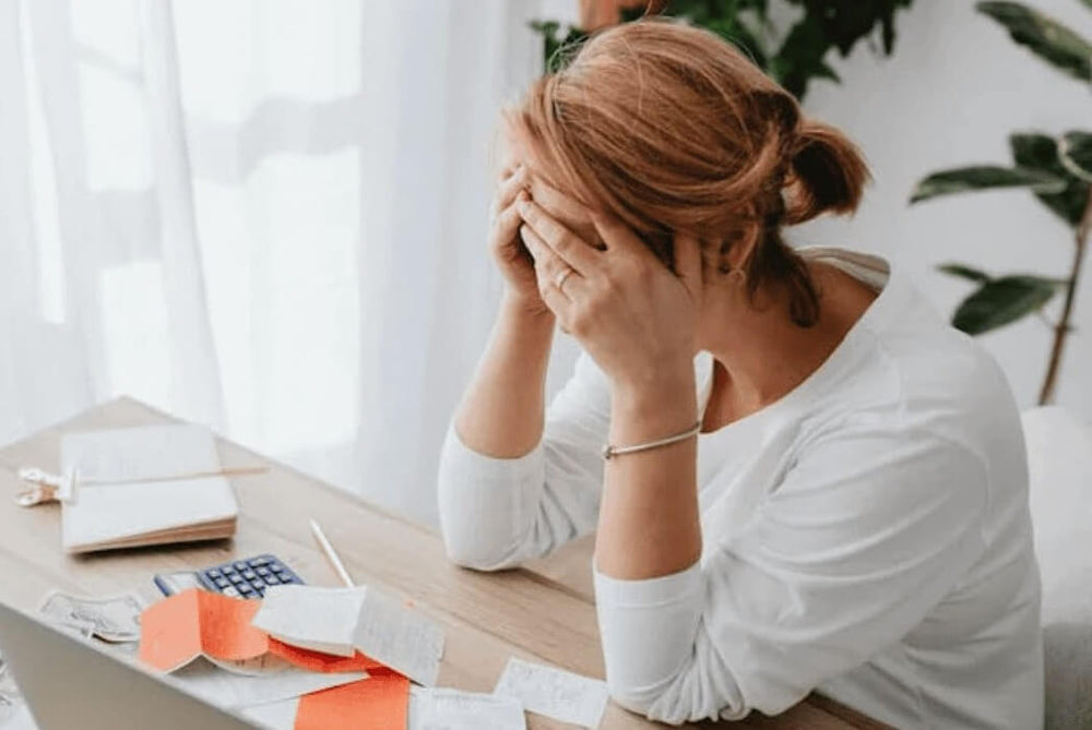 Donna stressata per problemi economici alla scrivania con bollette, ricevute e calcolatrice. Scena di ansia finanziaria prima di usare un budget planner Excel.